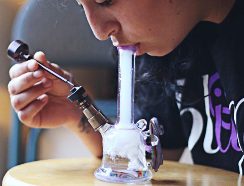 a woman using a small glass dab rig with a metal nail and dab tool